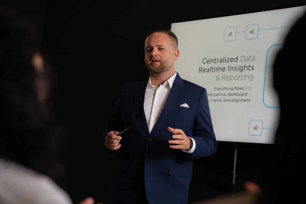 Troi Präsentationsfoto: Person im Anzug erklärt vor Screen mit „Centralized Data Realtime Insights & Reporting“ im Rahmen eines Vortrags